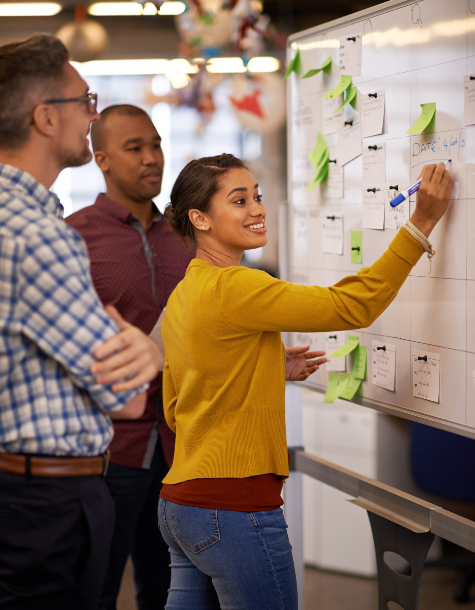 3 team members smile while working together placing ideas on a whiteboard